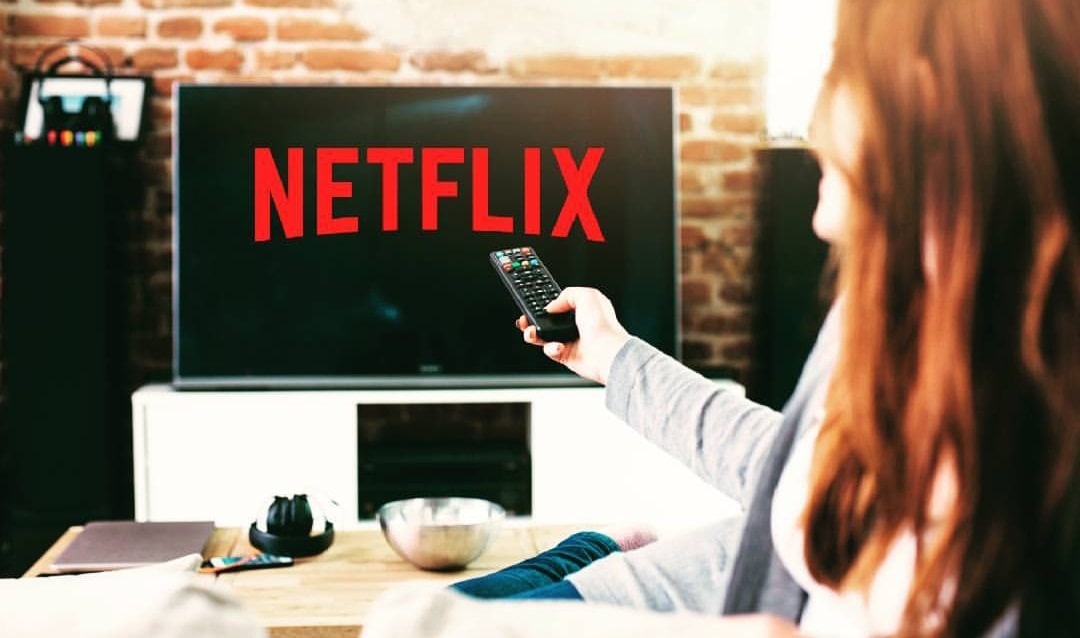 Televisão ligada nos filmes da Netflix - Mulher com controle na mão procurando um filme