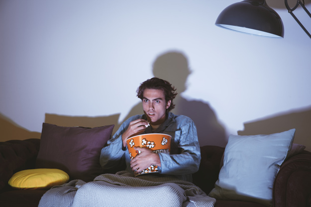 homem assistindo filme de terror sozinho na sala comendo pipoca