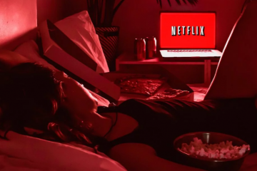 mulher deitada na cama assistindo filme na Netflix no notebook