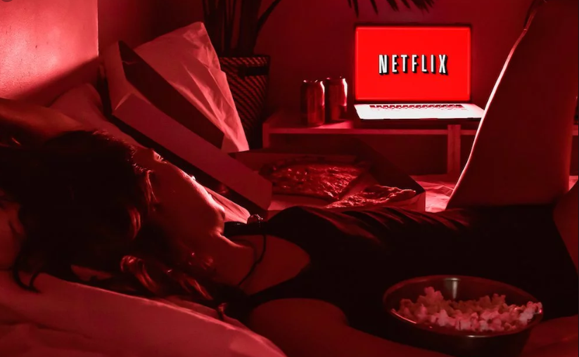 mulher deitada na cama assistindo filme na Netflix no notebook