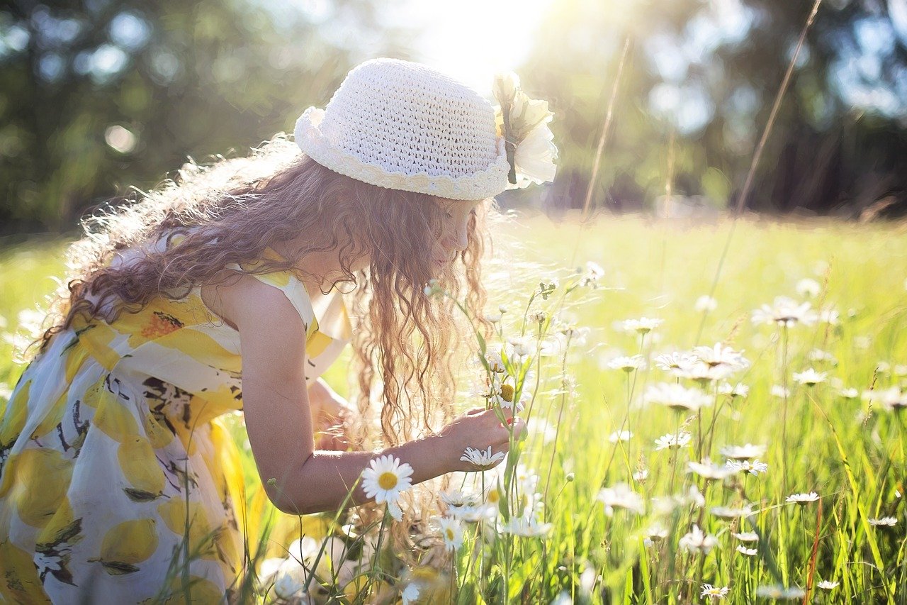 imagem de uma garota feliz em meio a um campo de flores com um chapéu branco