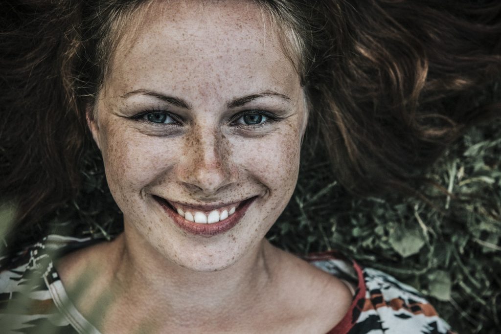 foto de uma mulher ruiva bonita com sardas sorrindo e deitada em um gramado