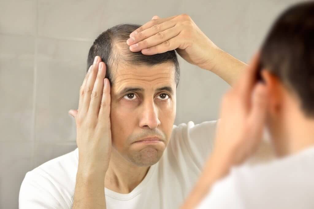 homem olhando as falhas no seu cabelo que caiu