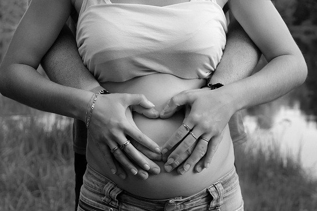 foto preta e branca de uma mulher grávida com o marido na mão da barriga